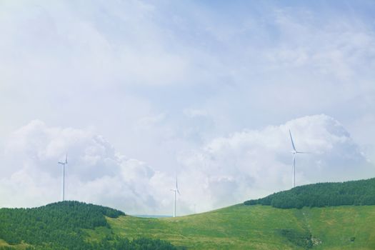 Wind turbines on lush, green, landscape with clouds.