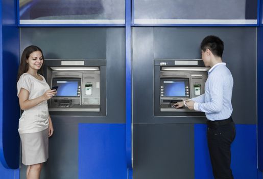 Two people standing and withdrawing money from an ATM