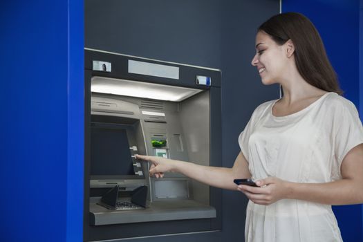 Smiling young woman withdrawing money from the ATM