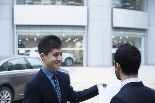 Car salesman holding car keys and paperwork and selling a car to a young businessman