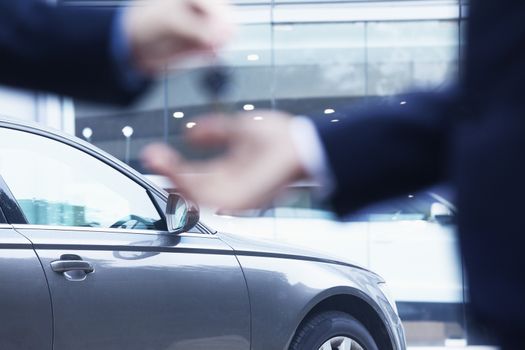 Car salesman handing over the keys for a new car to a young businessman, close-up 