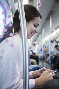 Young businesswoman sitting on the subway and using her phone