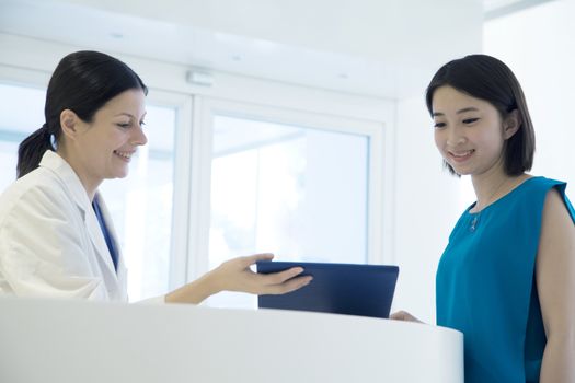 Smiling doctor and patient standing by the counter in the hospital looking down at medical record