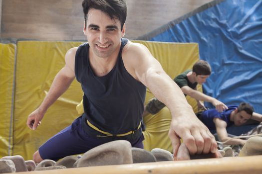 Smiling young man climbing up a climbing wall in an indoor climbing gym, directly above