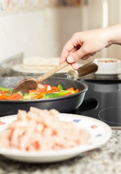Closeup of female cooking vegetables and chicken for a mexican food in a black pan
