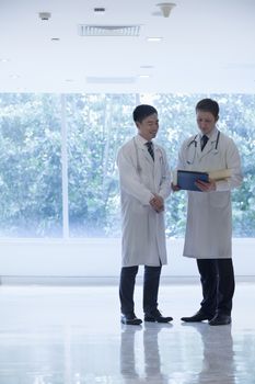 Two doctors standing, looking down, and consulting over medical record in the hospital