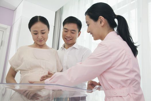 Nurse touching pregnant woman's belly in the hospital with husband beside her