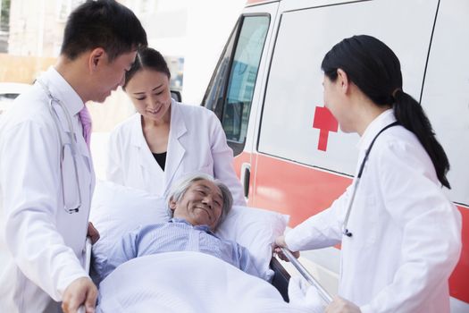 Three doctors wheeling in a elderly patient on a stretcher in front of an ambulance