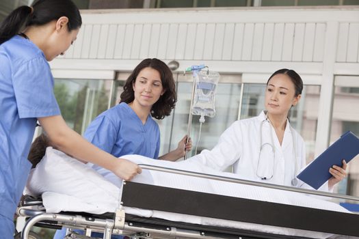 Female paramedics and doctor wheeling in a patient on a stretcher in front of the hospital