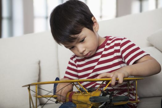 Little boy looking down and holding a model airplane,  on the couch in the living room