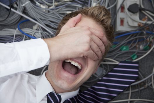 Frustrated man lying down covering his eyes surrounded by computer cables