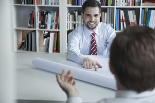 Two smiling architects discussing over a blueprint in the office, 