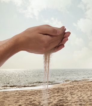 Hands holding and spilling sand with beach in the background