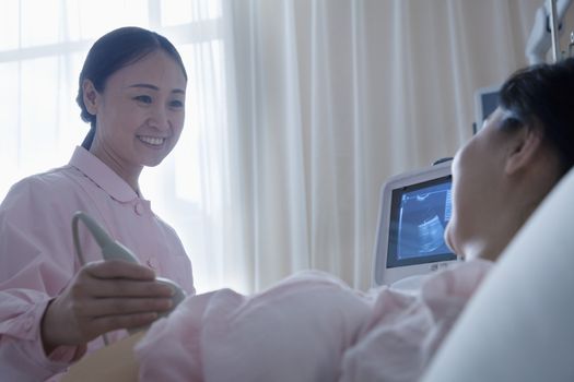Nurse doing an ultrasound on a pregnant woman lying on her back in the hospital