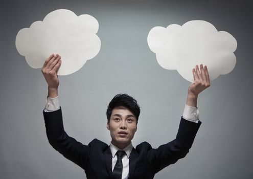 Businessman holding two paper clouds, studio shot