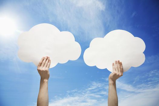 Person holding two cut out paper clouds against a blue sky with clouds