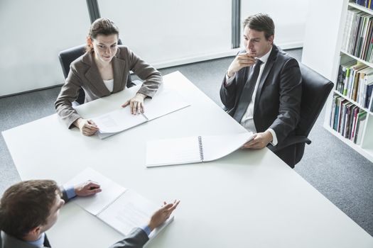 Three business people sitting around a table and having a business meeting, high angle view 