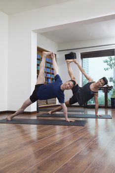 Two people with legs raised and arms outstretched doing yoga in a yoga studio