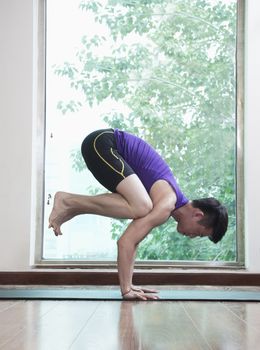 Man with legs off the ground and balancing in a yoga position in a yoga studio, side view