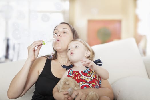 Mother and daughter sitting on the couch and blowing bubbles in the living room