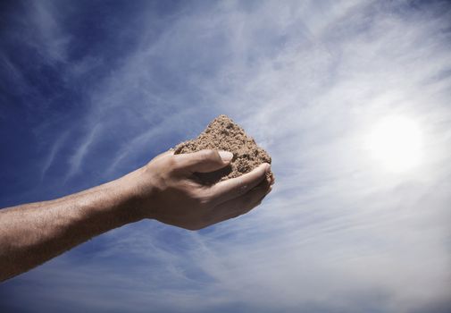 Hands holding a pile of soil with sun and sky in the background