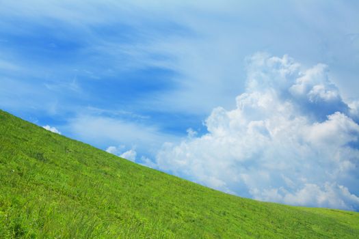 Lush, green hill with blue sky and clouds.