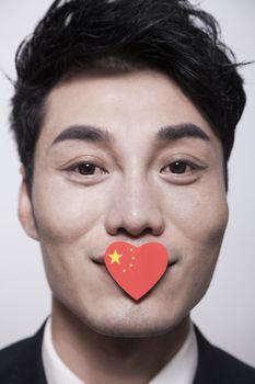 Young businessman looking at the camera with a heart shaped Chinese flag covering his mouth