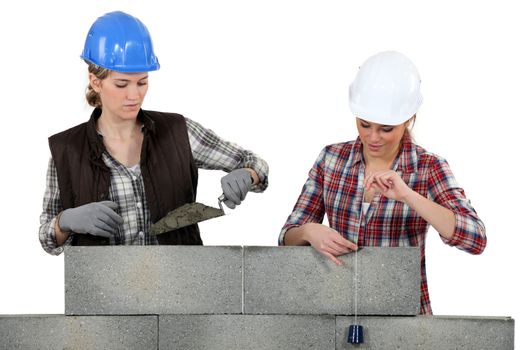 Two female mason working on a wall.