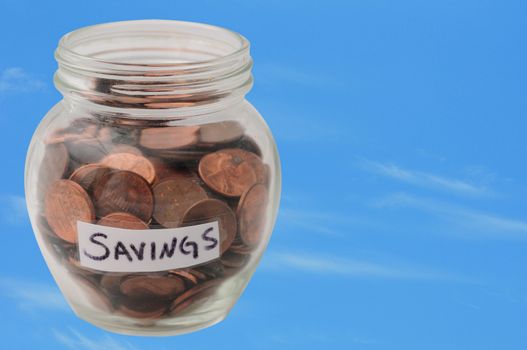 pennies in a savings jar on a blue sky for saving money concept
