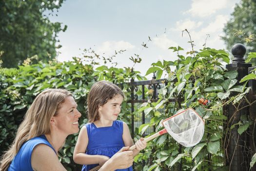 Smiling mother and daughter holding a butterfly and attempting to catch a butterfly in the garden