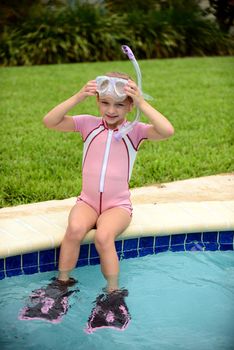 young girl sitting on edge of swimming pool in summer