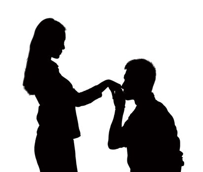 Silhouette of man on one knee, kissing woman's hand.