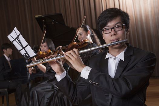 Flautist holding and playing the flute during a performance, looking at the camera