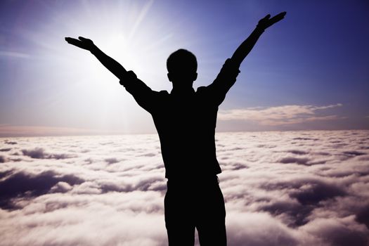 Silhouette of young man with arms raised with clouds and sky in the background