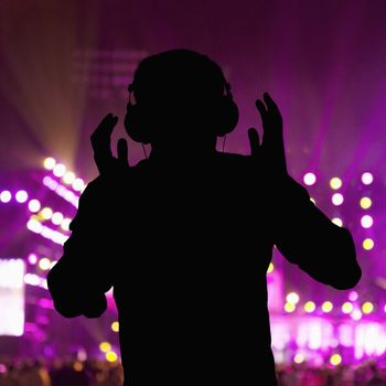 Silhouette of DJ wearing headphones and performing at a night club 