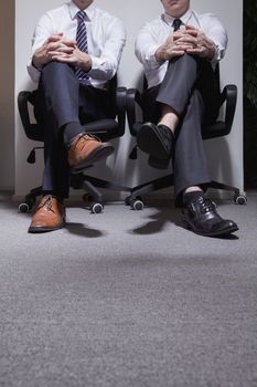 Two businessmen sitting down with legs crossed, low section