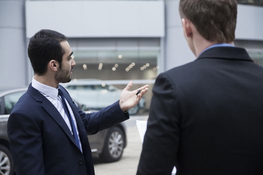 Car salesman holding car keys and selling a car to a young businessman