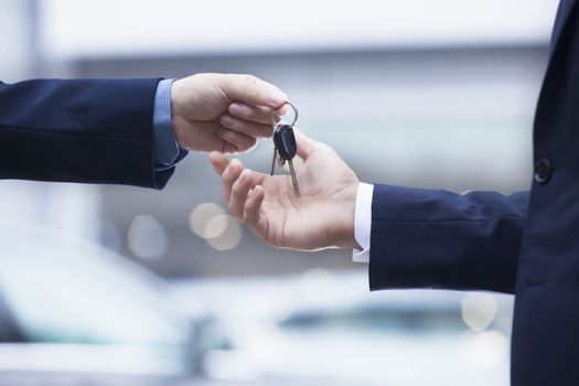 Car salesman handing over the keys for a new car to a young businessman, close-up 