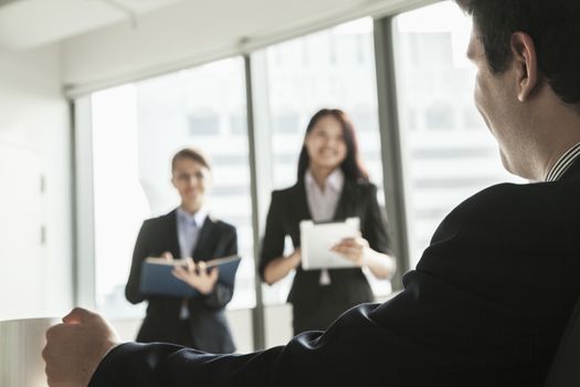 Two businesswomen standing up and presenting during a business meeting as a businessman watches