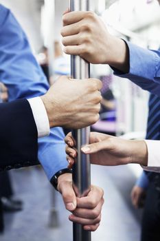Close-up of four business people's hands holding the pole on the subway
