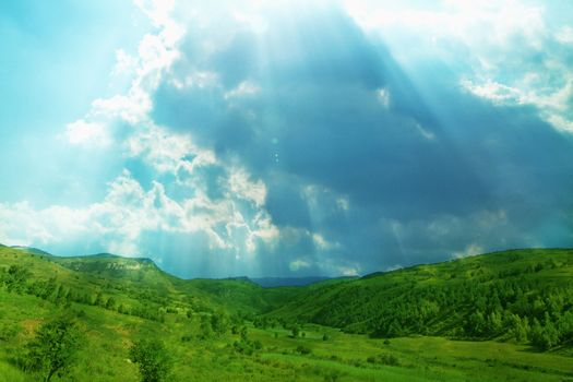 Lush, green landscape with sun shining through clouds.