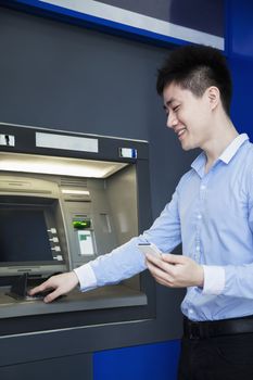 Smiling young businessman withdrawing money from the ATM