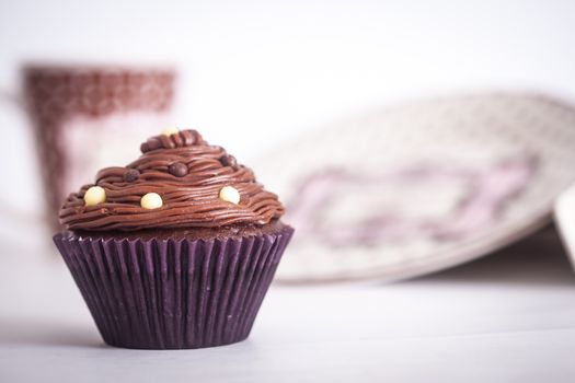 A cupcake in front of plates and a mug, on a white background.