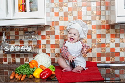 Baby cook with vegetables sits on a kitchen table