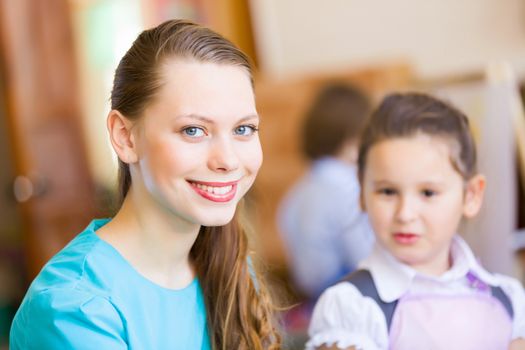 Little girl painting with teacher at kindergarten