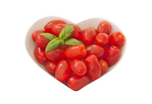 A bowl of baby plum tomatoes on a light coloured cloth. there is a sprig of basil in the top left hand corner to give a splash of green.