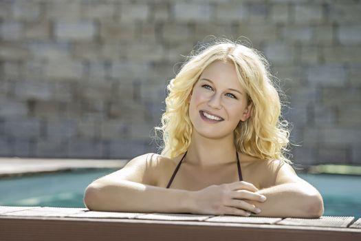 Portrait of a happy blond girl with blue eyes in a pool at the edge