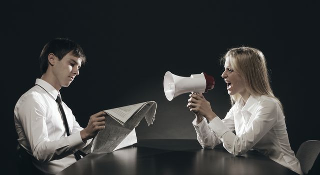 Girl with megaphone, shouting loudly, young man is reading a newspaper ignoring her