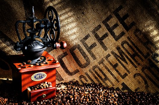 Cup of steaming hot coffee with coffee beans, coffee grinder, and coffee beans bag in background.