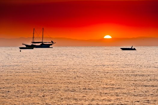 red sunset behind the mountains over the sea and ships